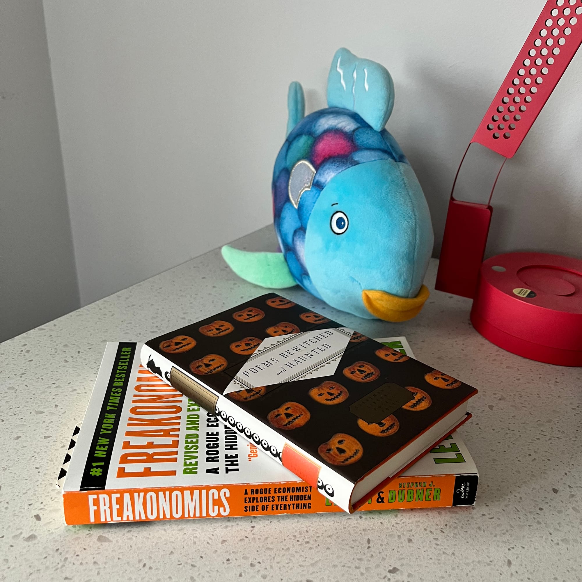 Two books lay atop one another with a plush fish and desk light situated behind them.